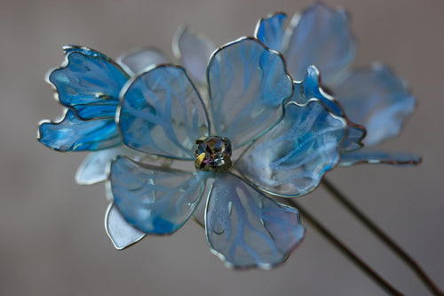 Close-up of translucent blue flowers on a bridal hair fork, showing painted petal veins and sparkling centres.