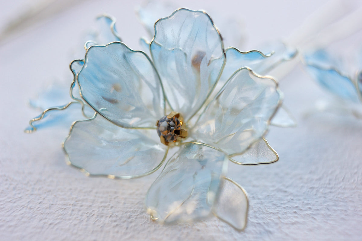 Pale blue translucent flower with fine petal outlines and a sparkling centre on a white background.
